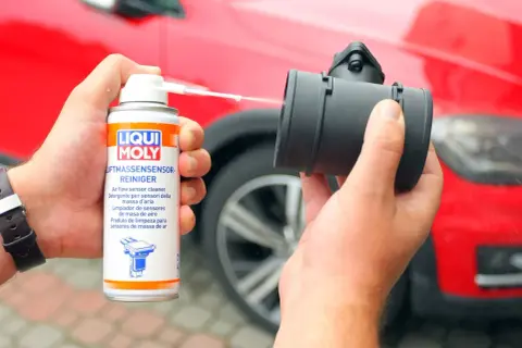 Czyszczenie przepływomierza preparatem Liqui Moly. Ręka trzyma puszkę z preparatem i aplikuje go na element.