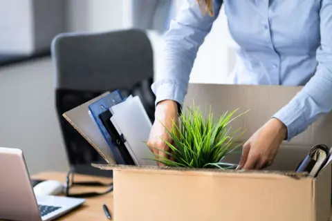 Frau packt ihre Bürosachen in einen Karton, um einen ausstand zu geben. Ein Laptop und Ordner sind zu sehen.