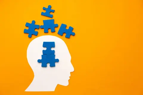 Blauwe puzzelstukjes vallen uit een witte hoofdvorm, sommigen boven, anderen in het hoofd. Het symboliseert het proces van het oplossen van gedachten, zoals bij pdd nos engels.