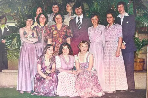 Grupa osób w eleganckich, pastelowych kreacjach. Widać długie suknie i garnitury, typowe dla lat 60 stylizacje.