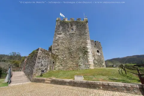 El castillo de Moeche, una imponente fortaleza de piedra, se alza bajo un cielo azul. Un puente de madera conduce a sus muros cubiertos de vegetación.