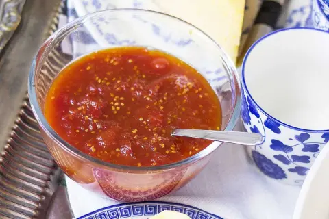 En skål med tomatmarmelad, perfekt för ett enkelt tomatmarmelad recept. Serveras med en sked och en blåvit kopp.
