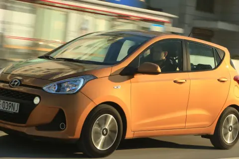 Pomarańczowy Hyundai i10 z kierowcą w środku jedzie ulicą.