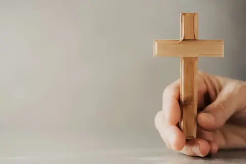 Eine Hand hält ein hölzernes Kreuz, ein Symbol, das Christen weltweit verbindet.