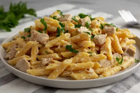 Penne con pollo w kremowym sosie, posypane świeżą natką pietruszki. Pyszne danie gotowe do podania.