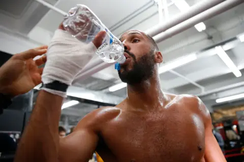 A boxer, hand-wrapped, drinks from a water bottle. This shows why boxers spit out water: to stay hydrated without swallowing too much.