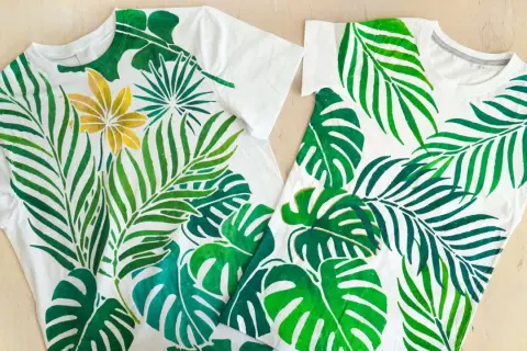 Deux t-shirts blancs ornés de motifs de feuilles tropicales peintes à la peinture acrylique sur tissu. Une touche de doré sur une fleur.