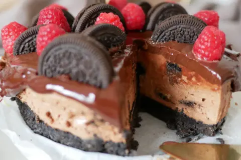 En chokladig oreo cheesecake med hallon och chokladglasyr. En bit är bortskuren.
