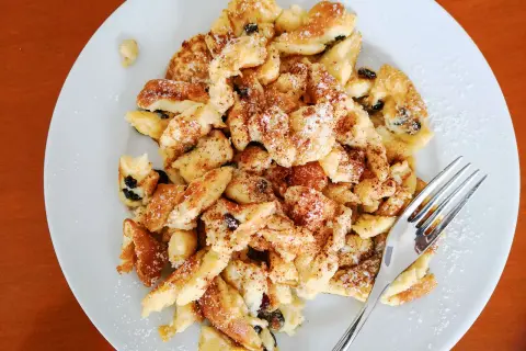 Ein Teller mit fluffigem Kaiserschmarrn mit Eischnee, bestreut mit Puderzucker und Zimt. Daneben eine Gabel.