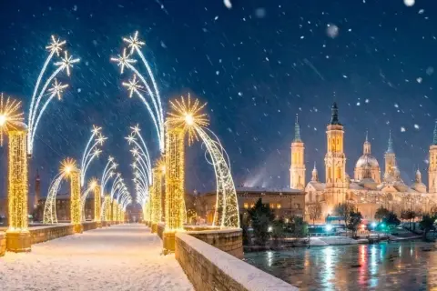 Puente nevado con encendido luces navidad Zaragoza. La Basílica del Pilar brilla bajo la nieve.