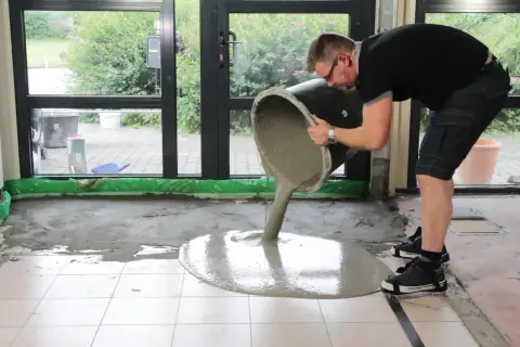 Mann gießt flüssigen Estrich aus einem Eimer, um den Boden auszugleichen.