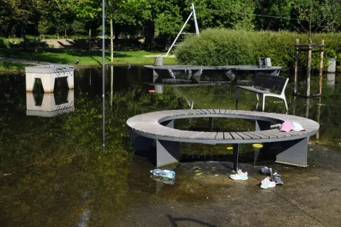 W parku wodziczki woda zalała ławki i stoły. Dzieci zostawiły buty i czapki, a butelka pływa po wodzie.