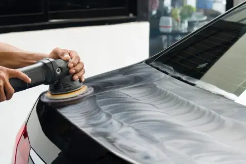 Mani esperte lucidano la lucida carrozzeria auto con una lucidatrice, creando un effetto specchiato.