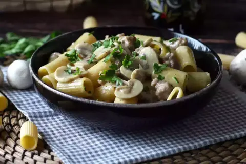 A bowl of rigatoni pasta with creamy mushroom and sausage sauce, garnished with parsley.