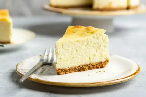Pyszny kawałek sernika z wiaderka na talerzyku, z widelcem. Idealny na deser po obiedzie.