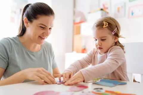 Bambina e maestra giocano con i puzzle in un asilo nido.
