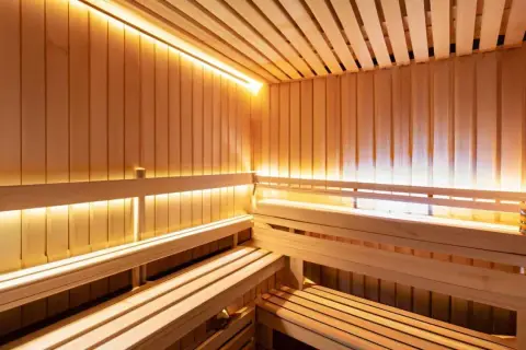 Drewniana sauna z ławami i ciepłym, nastrojowym oświetleniem. Lampy do sauny tworzą relaksującą atmosferę.