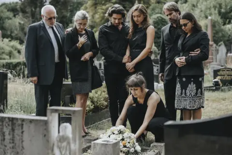 Trauernde Familie in schwarzer Beerdigungskleidung legt Blumen nieder.