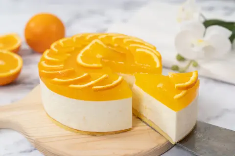 Sernik pomarańczowy z mascarpone, ozdobiony plasterkami pomarańczy, wygląda apetycznie. Kawałek ciasta został już odkrojony.