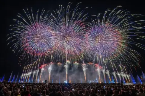 Spectacle de feu d'artifice sur le lac d'Annecy, illuminant le ciel nocturne de gerbes colorées au-dessus d'une foule admirative.