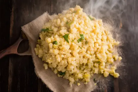 Gorąca kasza bulgur gotowanie na drewnianym stole, parująca i ozdobiona zielonymi ziołami.