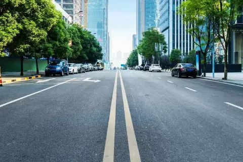 Eine Straße mit einer **durchgezogenen Linie** in der Mitte, gesäumt von Bäumen und modernen Gebäuden. Autos parken am Straßenrand.
