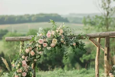 Un arc en bois rustique orné de roses roses et de verdure, parfait pour une cérémonie laïque champêtre.