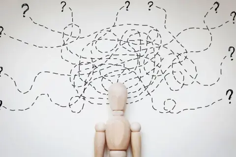 Drewniany manekin z chaotycznymi liniami i znakami zapytania nad głową, symbolizującymi trudności w diagnozie, np. borderline ICD 10.