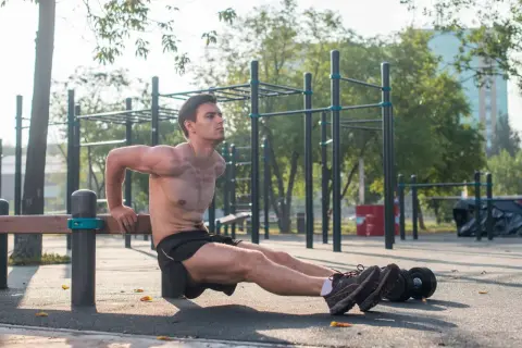 Mężczyzna wykonuje pompki na triceps na ławce na siłowni plenerowej.