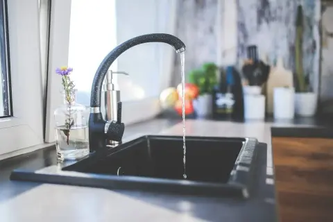 Un robinet noir verse de l'eau dans un évier, suggérant la filtration eau du robinet pour une boisson pure et saine.