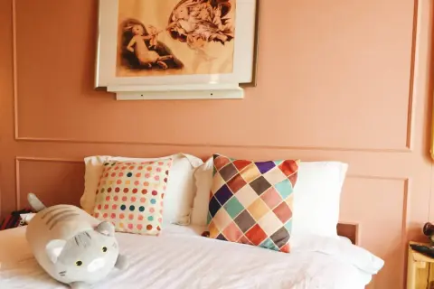 Chambre couleur terracotta avec un lit douillet, des coussins colorés et une peluche chat. Un tableau de lapins orne le mur.
