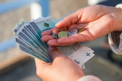 Dłonie liczą pieniądze, symbolizując oszczędności na przyszłość, być może związane z wiekiem emerytalnym kobiet.