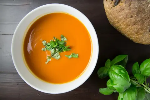 Aksamitna pomidorowa z ryżem, udekorowana świeżą bazylią, obok chrupiącego bochenka chleba.
