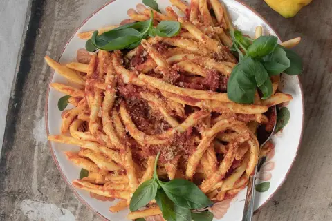 En skål med nduja pasta, toppad med färsk basilika och en citron i bakgrunden.