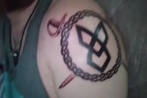 Tatuaże wikingów na ramieniu: pleciony łańcuch, miecz i symbol.