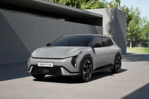 Nowy Kia EV4 GT-Line w kolorze srebrnym, zaparkowany przed nowoczesnym budynkiem z zielenią w tle.