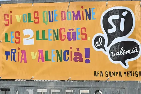 Cartel naranja con letras de colores: "Si vols que domines les llengües, tria València!". Promociona cursos homologados en València.