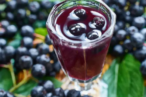 Aronia w kieliszku, jak nalewka z aronii przepis babci. Wokół świeże owoce i liście.