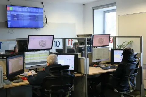 Operatorzy 112 pracują w centrum dowodzenia, monitorując sytuację na mapach i danych.