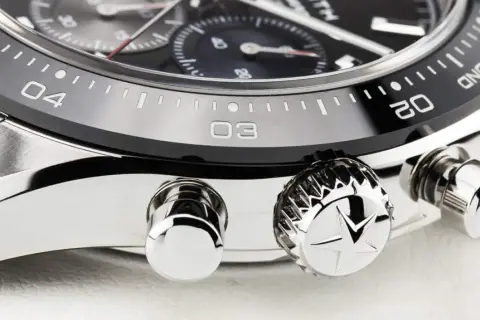 Detalle de un reloj de lujo, mostrando el bisel con números y marcas, y los pulsadores. El bisel del reloj está diseñado para cambiar la hora.