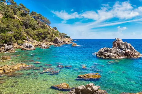 Piękna pogoda w Lloret de Mar w czerwcu. Turkusowa woda, skaliste wybrzeże porośnięte zielenią, błękitne niebo z chmurkami.