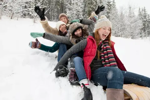 Des amis s'amusent en luge dans la neige, une scène joyeuse typique d'Annecy en décembre.