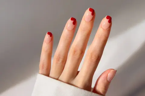 Une main aux ongles nude ornés de petits cœurs rouges. Une idée ongle coeur parfaite pour la Saint-Valentin ou pour ajouter une touche d'amour à votre quotidien.