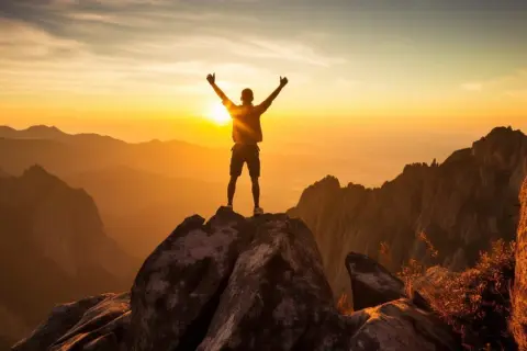 Hombre en la cima de una montaña al amanecer, celebrando su **crecimiento personal y espiritual**.