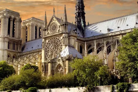 Katedra Notre Dame w Paryżu z różanymi oknami i wieżami na tle pomarańczowego nieba.
