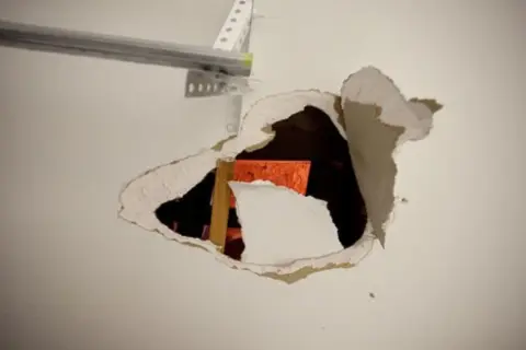 Un **buco nel muro troppo grande** rivela una struttura arancione e un montante di legno.
