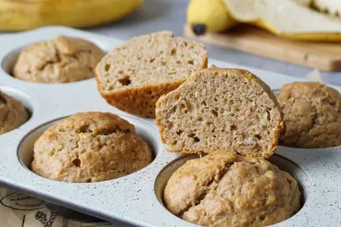 Saftige bananenmuffins ohne zucker, gebacken in einer Muffinform. Eine Hälfte ist aufgeschnitten und zeigt die lockere Krume.