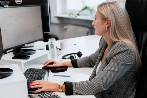 Kobieta w biurze pracuje przy komputerze, skupiona na zadaniach. To jej praca z norweskim, która wymaga precyzji i zaangażowania.