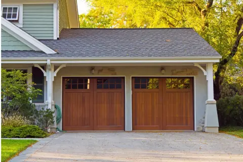 Doppio garage con porte in legno scuro, un box di pertinenza si può vendere separatamente. Alberi autunnali sullo sfondo.