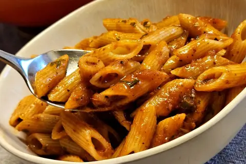 Eine Löffelportion Penne all'Arrabiata, mit einer würzigen Tomatensauce und Kräutern, wird aus einer Schüssel gehoben.